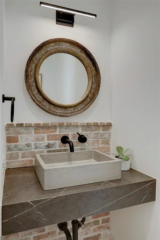 Bathroom vanity with a vessel sink, dark stone countertop, brick backsplash and round mirror. Custom Bathroom Counters  Houston, ‪Tx 713-568-5758‬
