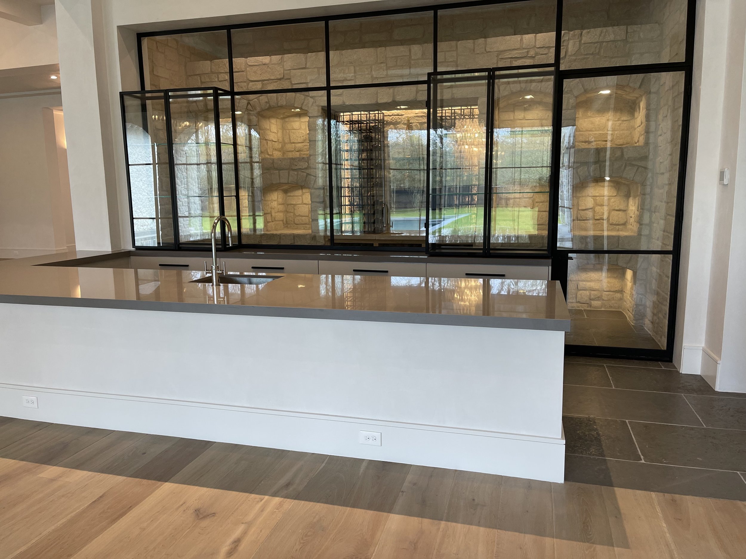 White waterfall counter beside black-framed glass cabinetry in a modern Houston kitchen. Texas Kitchen Countertops, ‪713-568-5758‬