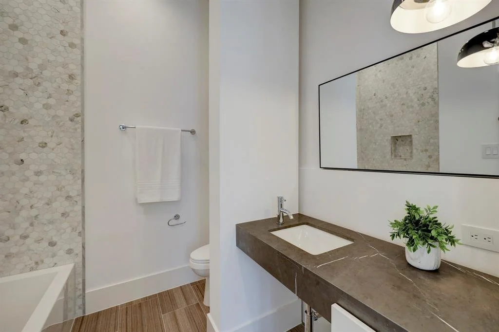 Modern bathroom with a dark stone vanity countertop, undermount sink and pebble tile shower in Houston, TX.