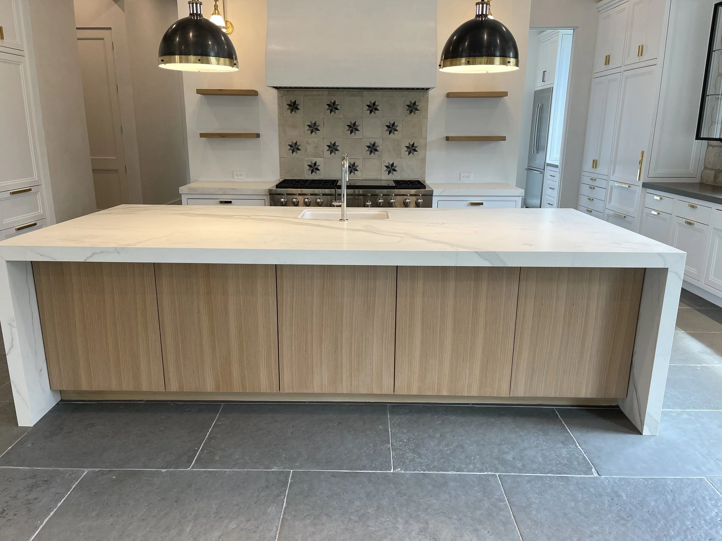 Modern kitchen with a white stone island, natural wood cabinetry, dark tile flooring and pendant lights.  Custom Kitchen Countertops Houston, ‪713-568-5758‬