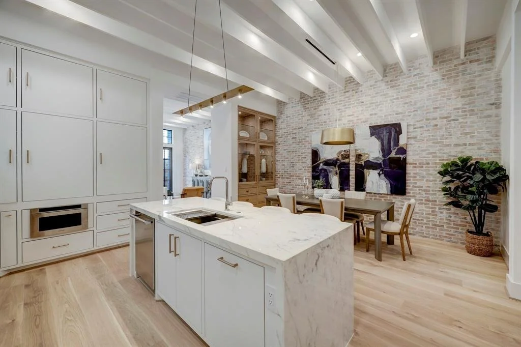 White kitchen with a custom stone island, white cabinetry and a brick accent wall in Houston, TX.