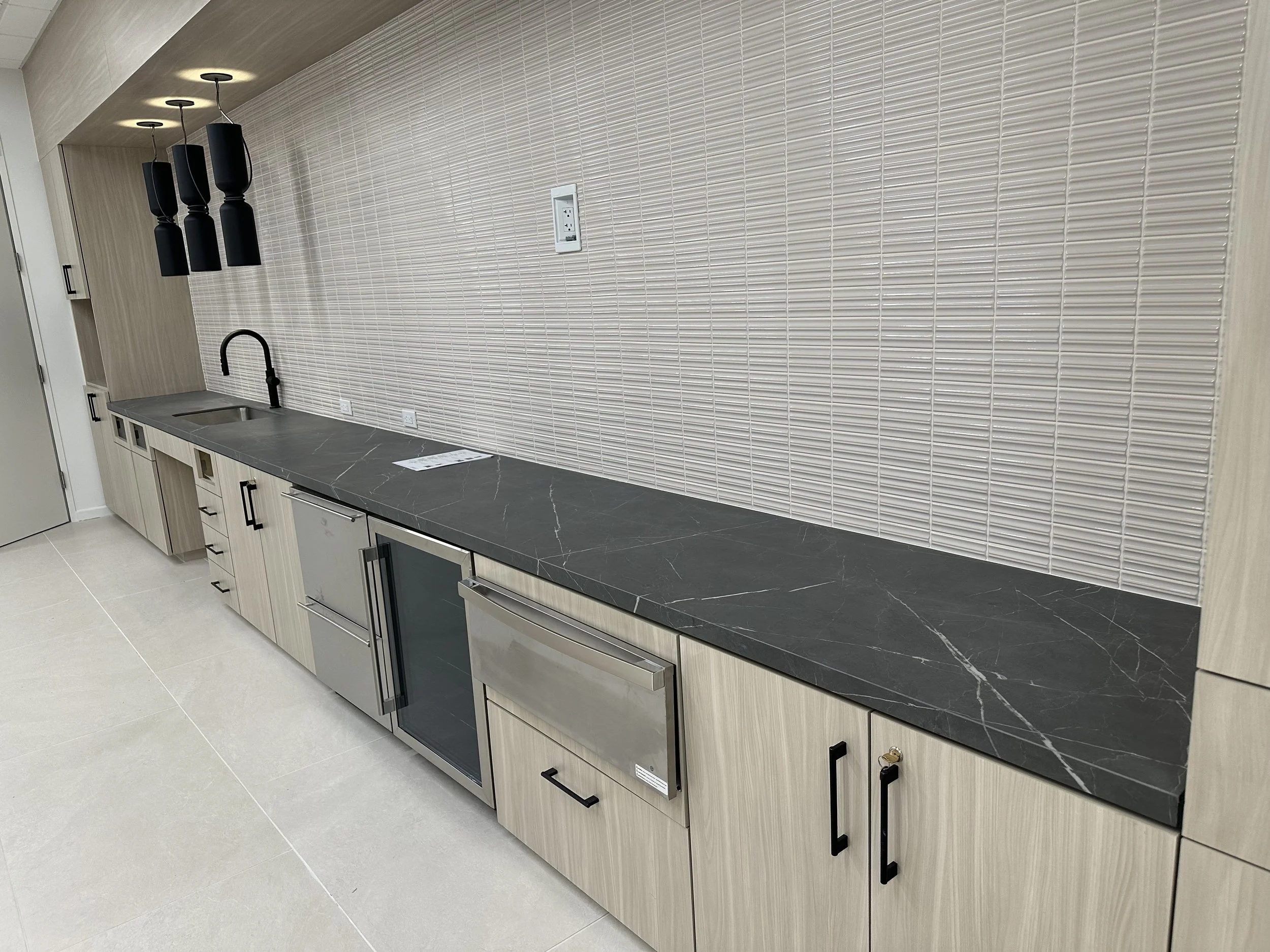 Commercial black stone countertop with light wood cabinetry and tile backsplash installed by Supreme Stone in Houston.