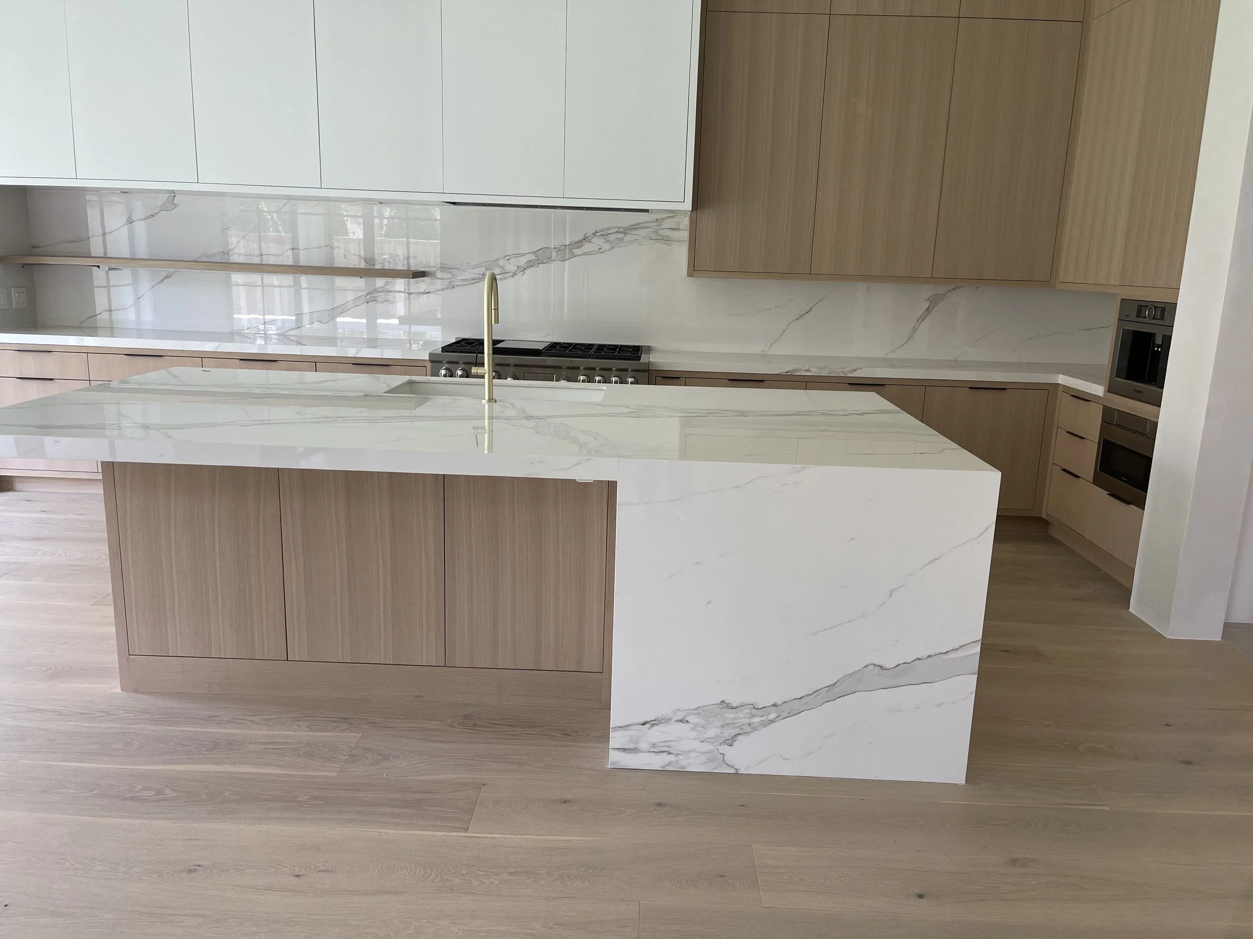 White waterfall-edge kitchen peninsula with natural wood cabinetry and matching backsplash. Custom Granite, Quartz, Porcelain Countertops, Woodlands Texas ‪713-568-5758‬