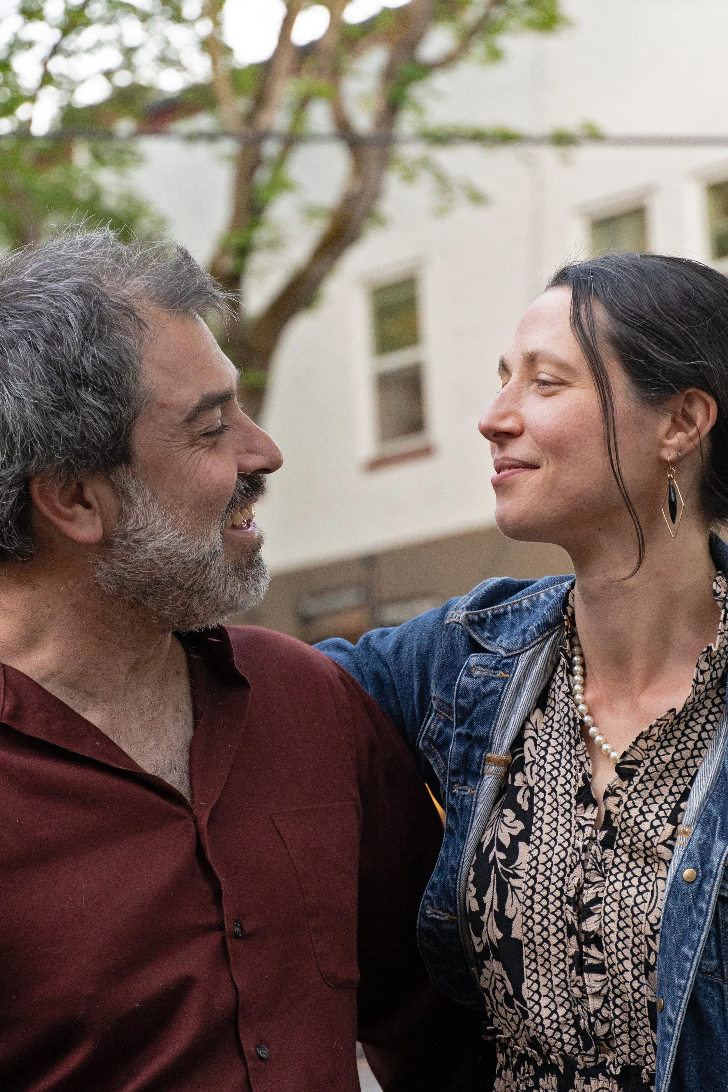 Massage therapist Eric Fair-Layman (left) and Craniosacral Therapist Erin Boyt (right) looking toward each other, smiling. They are outside on a beautiful day in late spring.