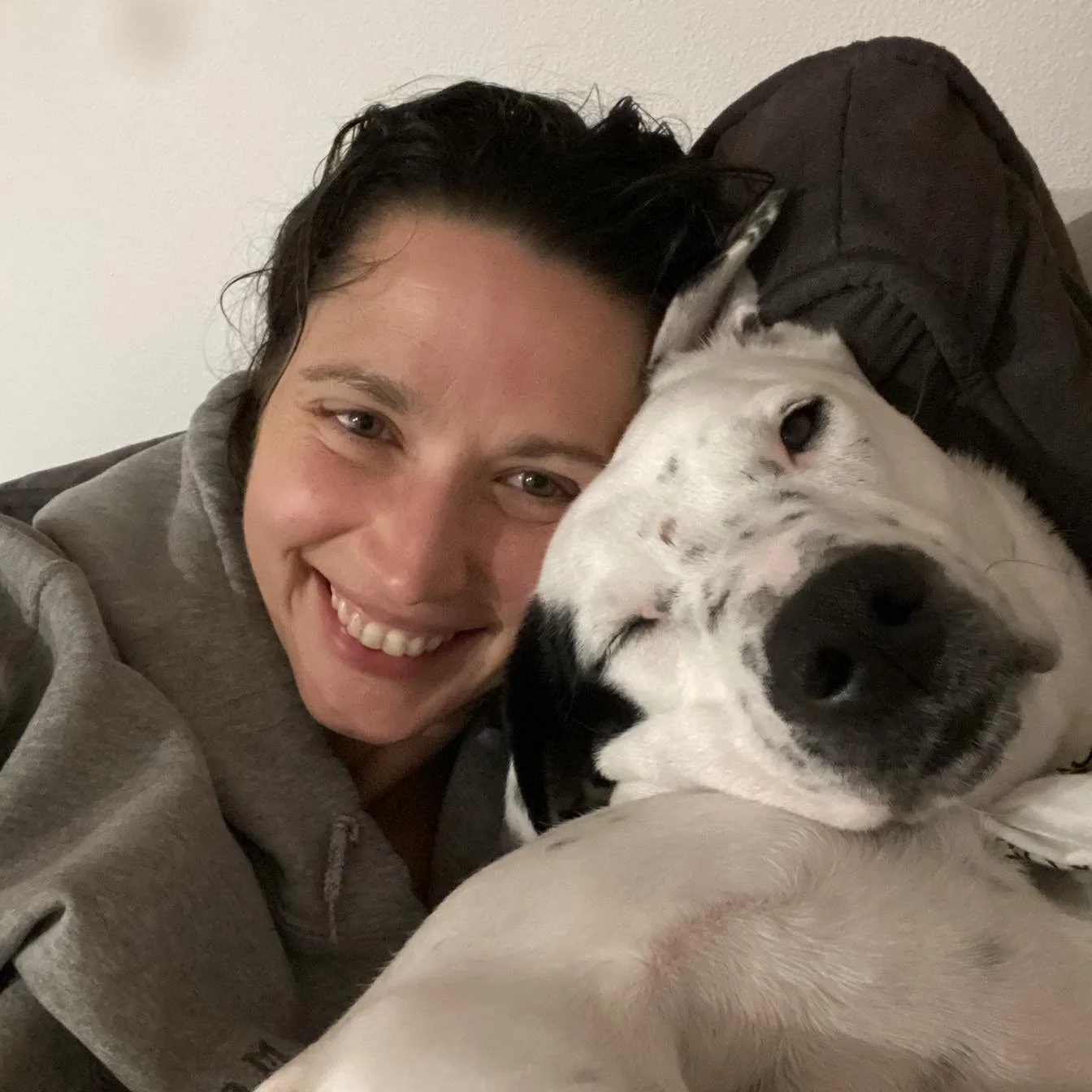 Closeup of Erin snuggling with her dog, Harlequin, and smiling. Harlequin is a white dog with black spots, black nose, and a black right ear.