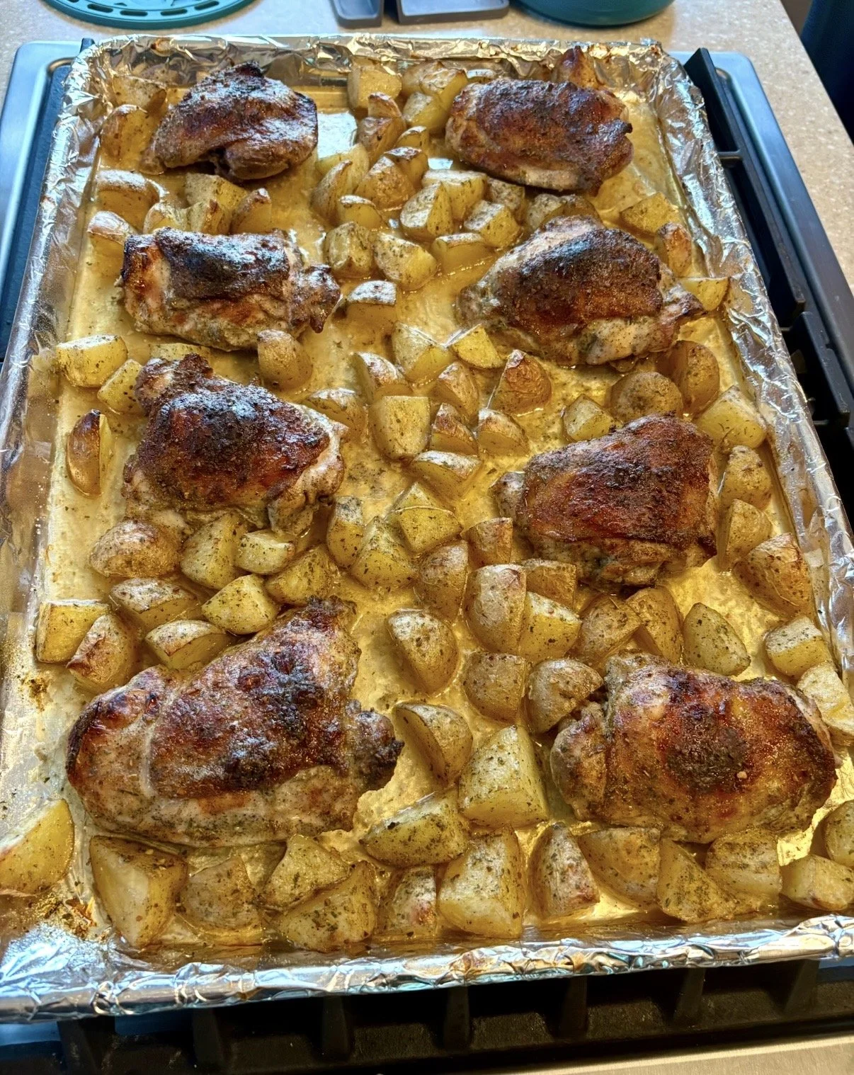 Baked chicken thighs with roasted potatoes on a foil-lined baking sheet.