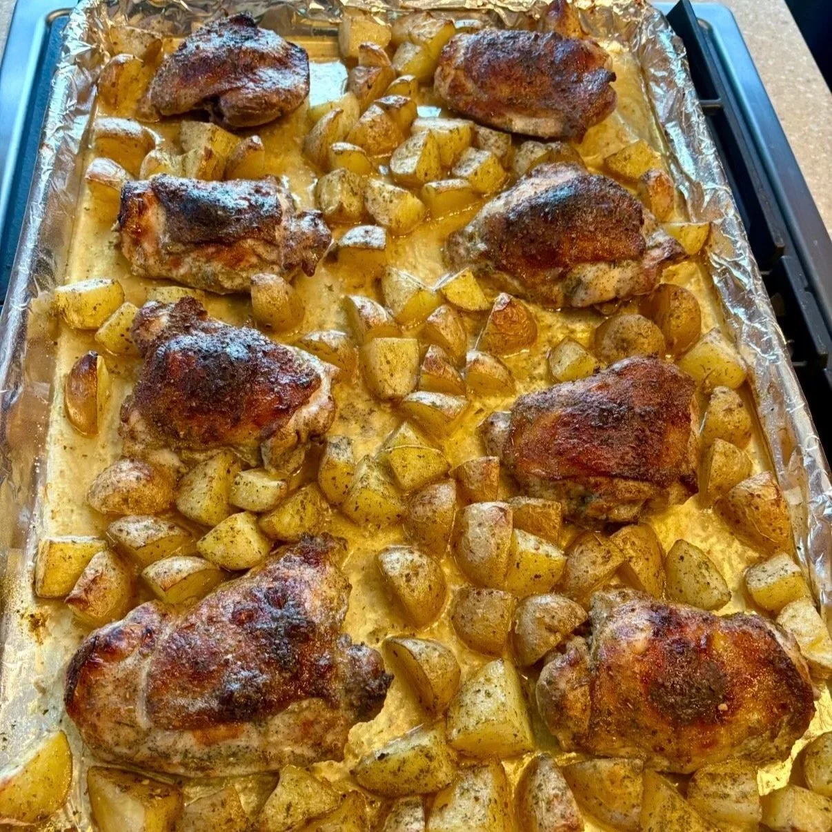 Baked chicken thighs with roasted potatoes on a baking sheet covered with aluminum foil.