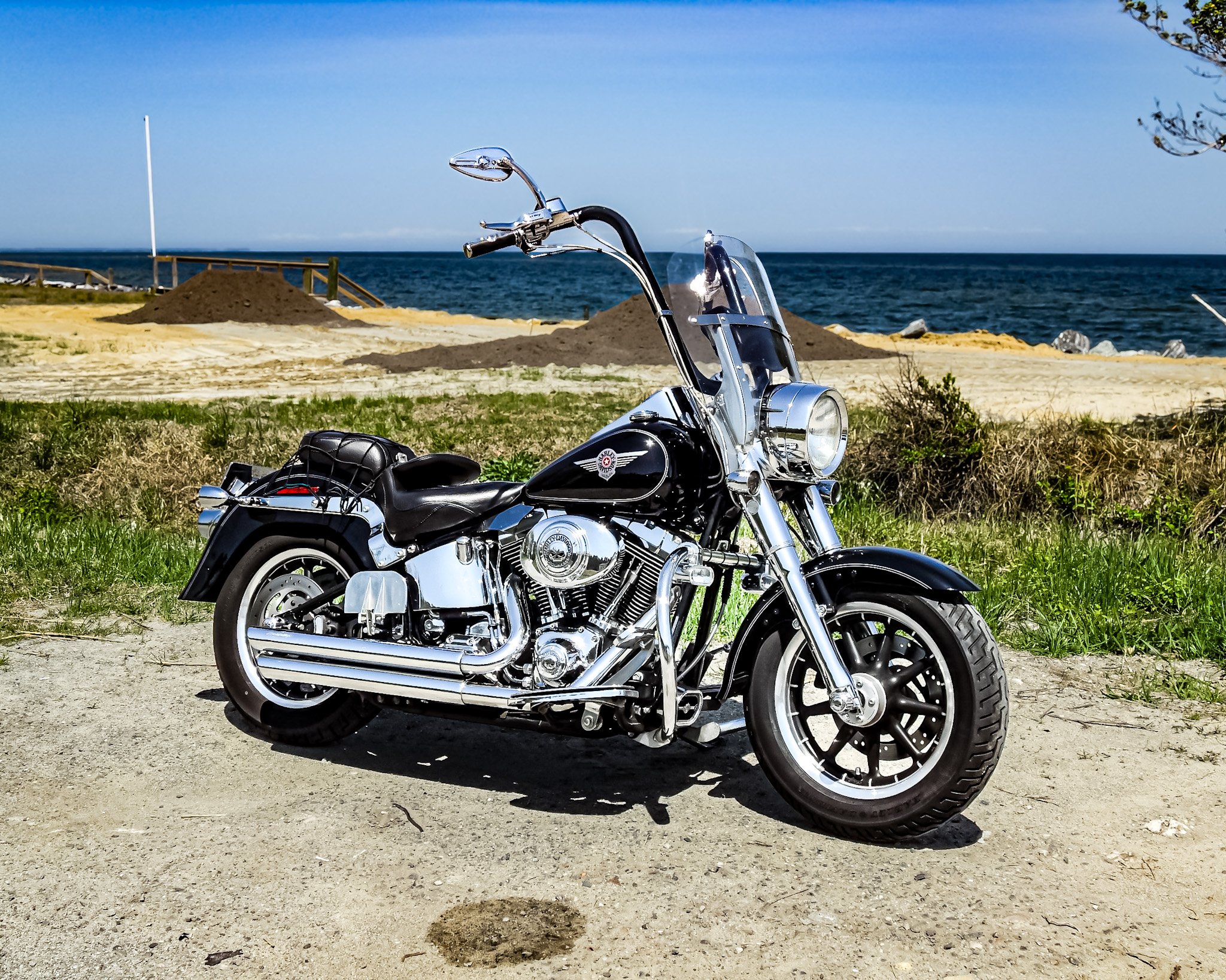 The perfect pit stop. My Harley’s black paint and polished chrome are catching the coastal sun, parked right on the edge of the sand.  Looking past the bike, it’s just miles of deep blue water meeting an endless clear sky.