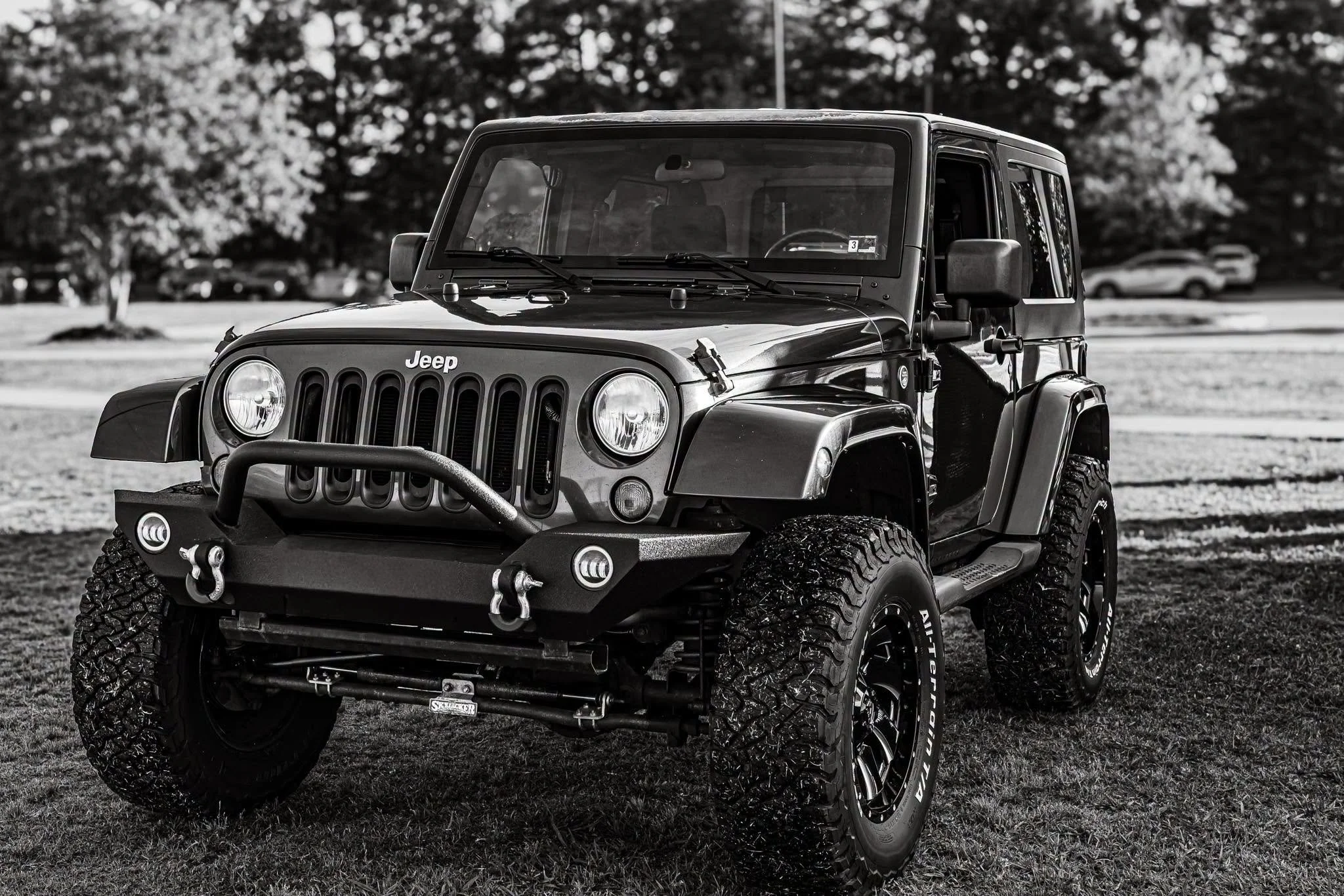 My Jeep, standing proud in a classic Black and White frame. Seeing it parked up on the grass against a backdrop of woods really highlights the stance—those aggressive off-road tires are ready for absolutely anything. It’s not just a vehicle; it’s a t