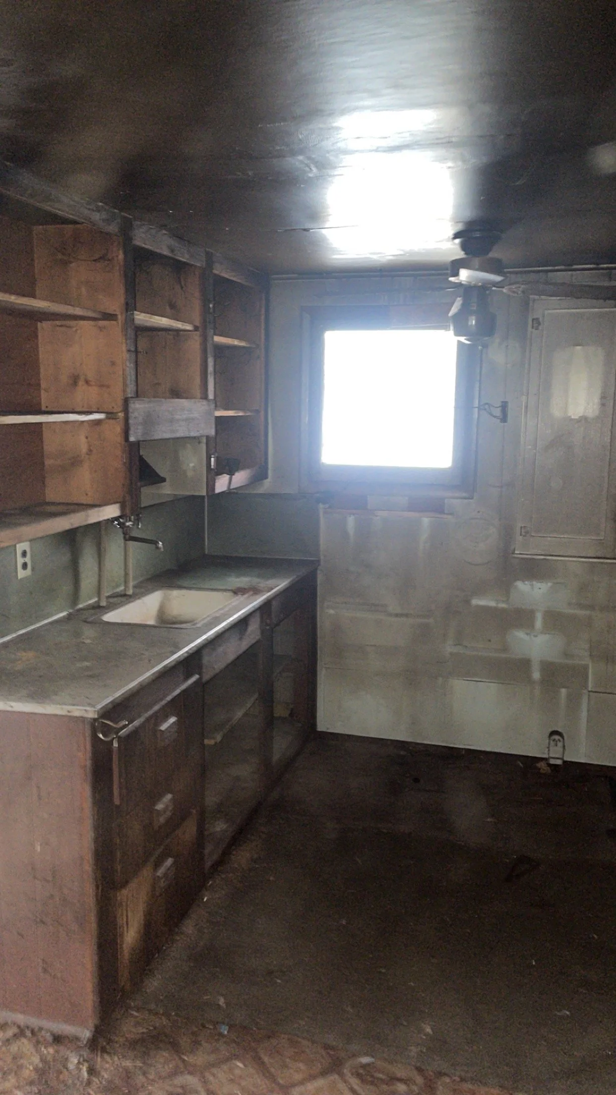 Old, abandoned kitchen with weathered countertops, empty cupboards, and exposed pipes.