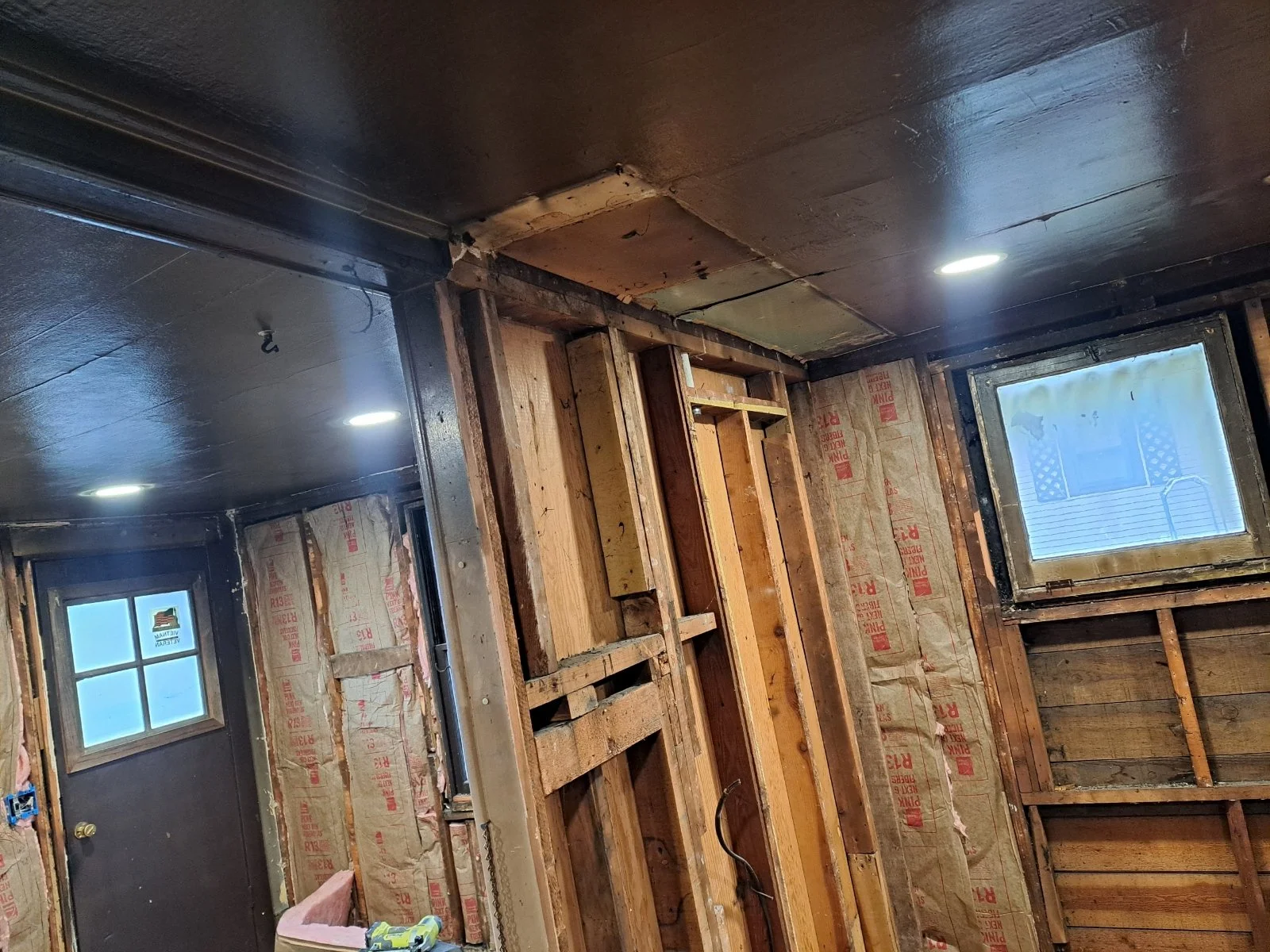 Room under renovation with exposed wooden framing, insulation, and small windows.