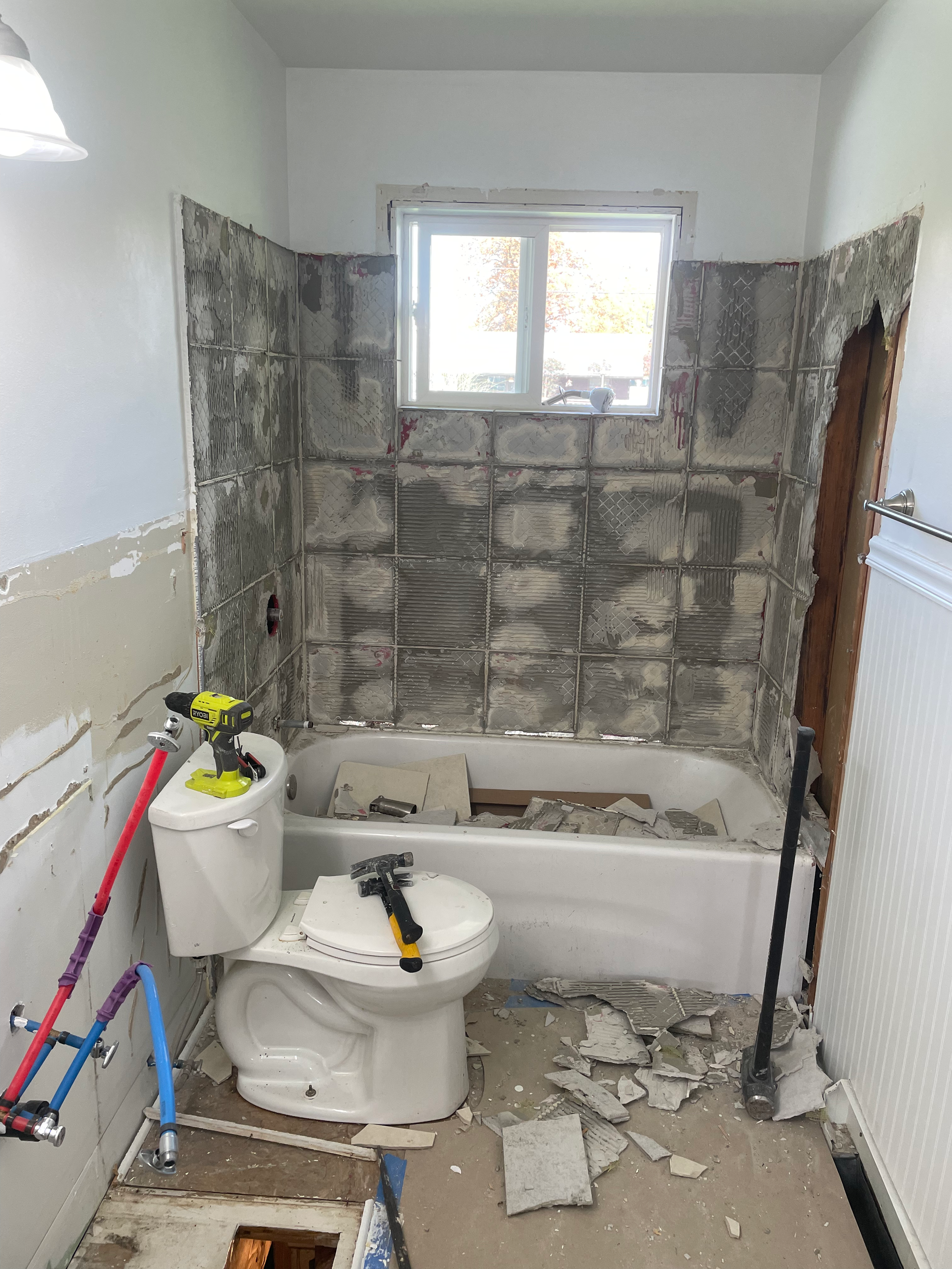 Bathroom under renovation with exposed walls, removed tiles, and construction tools on a toilet.