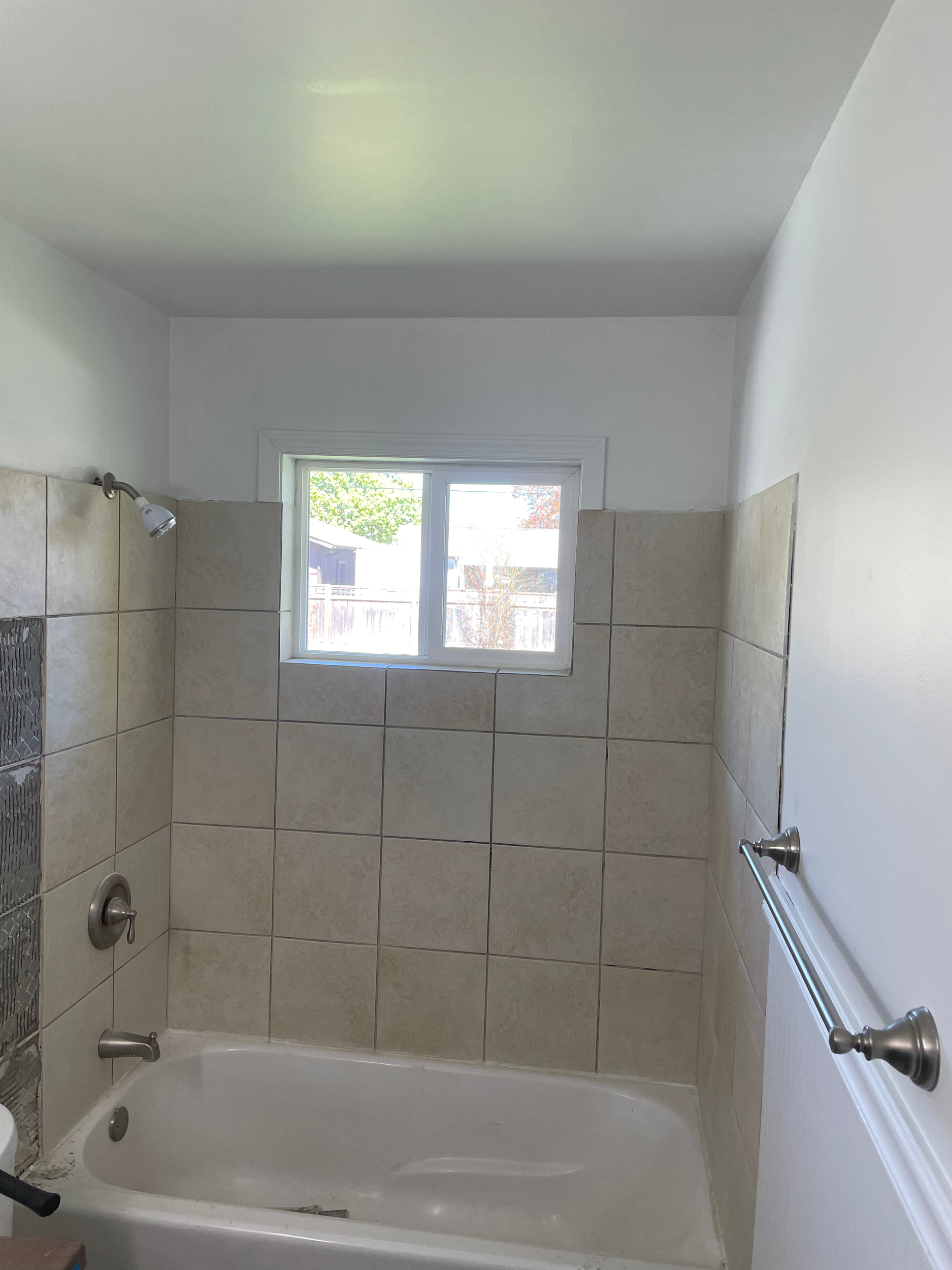 Bathroom with beige tiled walls, white bathtub, window, and showerhead.