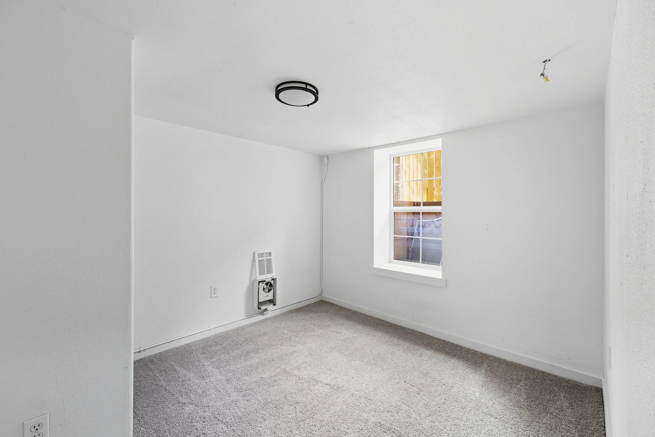Empty room with white walls, a window, carpeted floor, ceiling light fixture, and an air vent with ductwork.