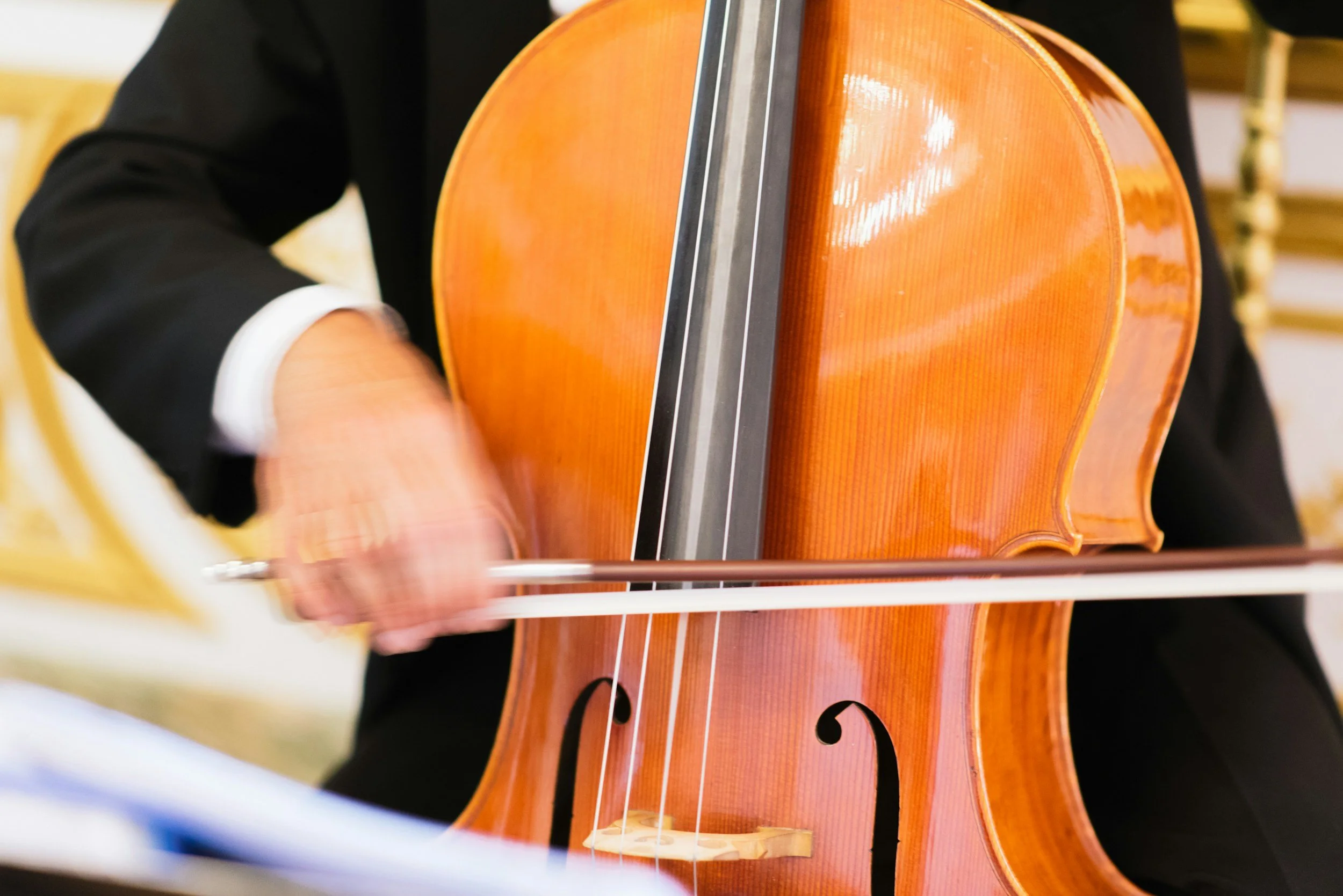 Close-up of a person playing a wooden cello, focusing on the side and fingerboard.