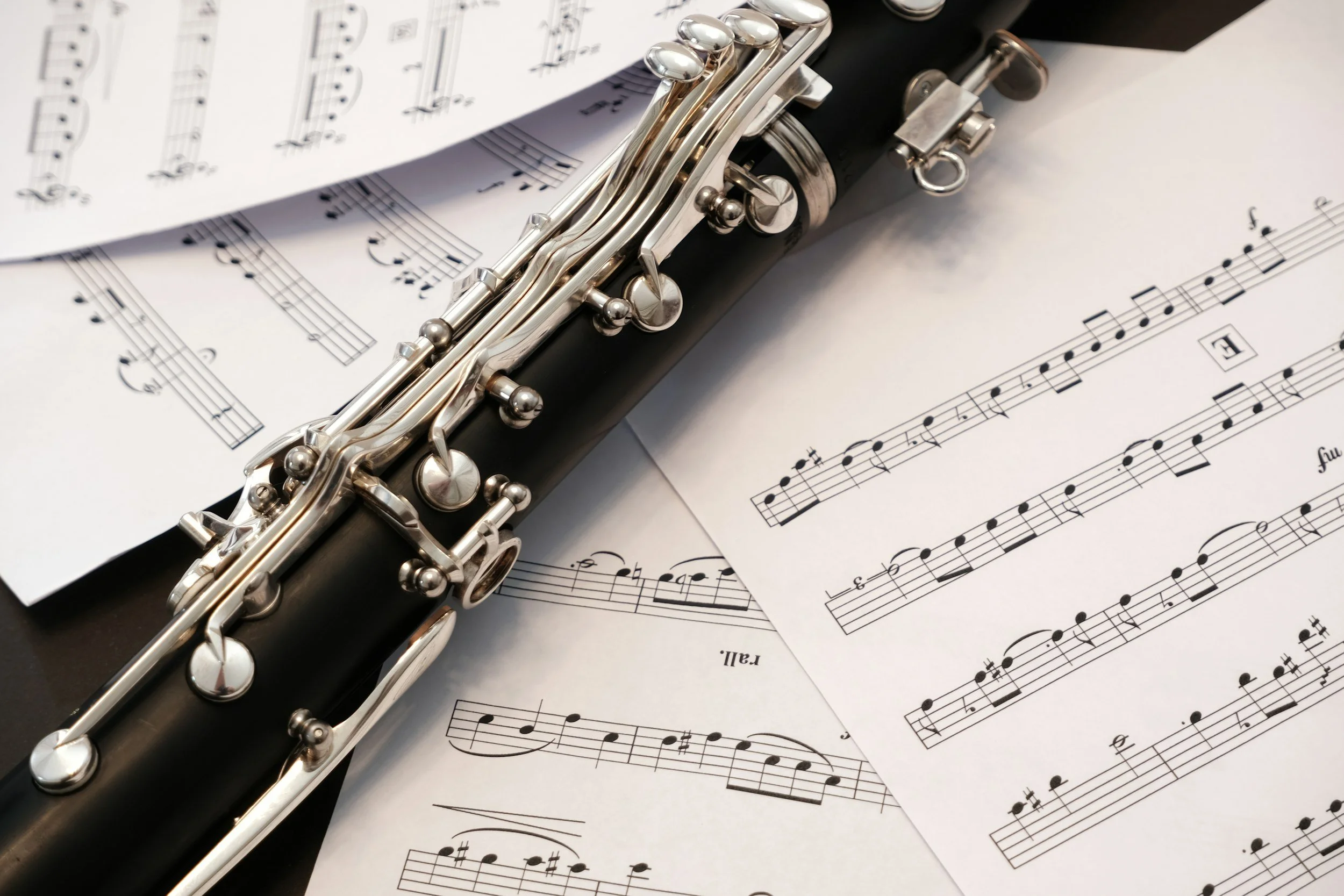 A close-up of a black and silver flute placed on sheet music papers with musical notes and notation.