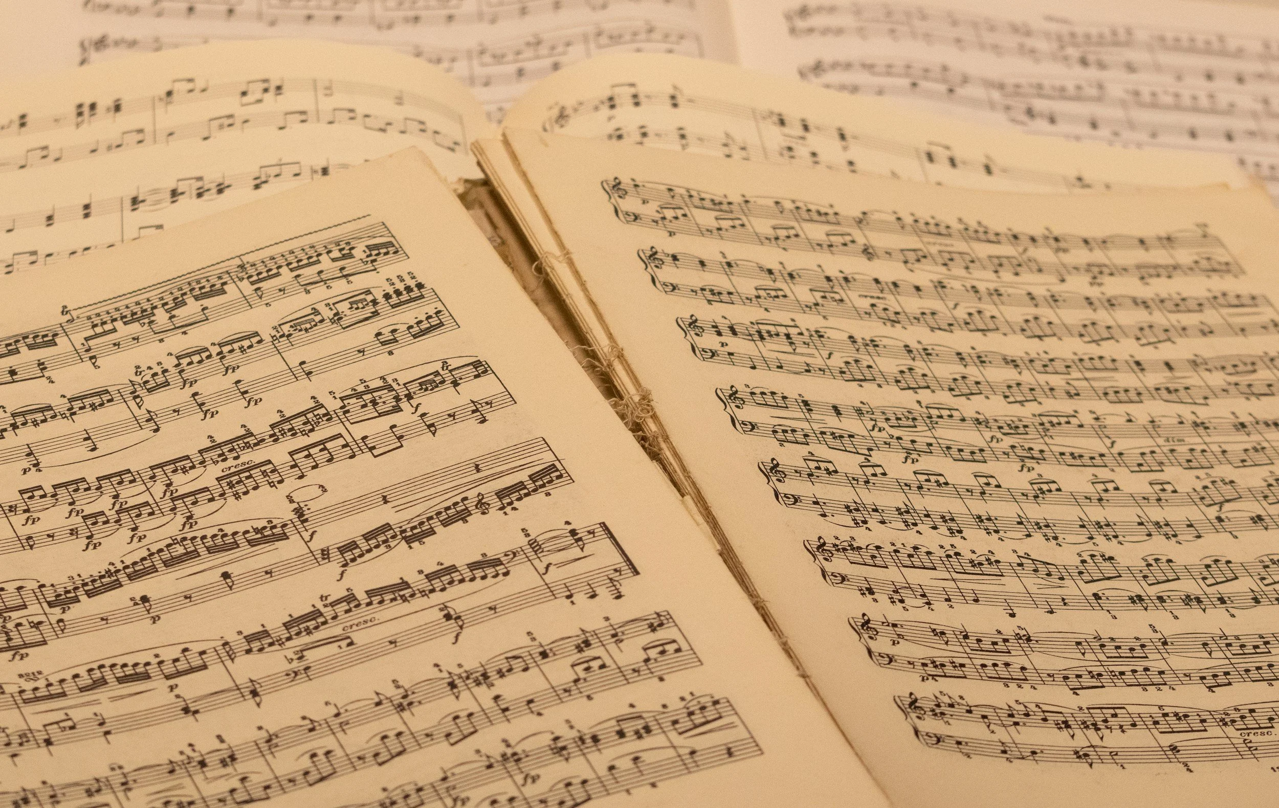 Open pages of a sheet music book with musical notation on cream-colored paper, partially overlapping each other.