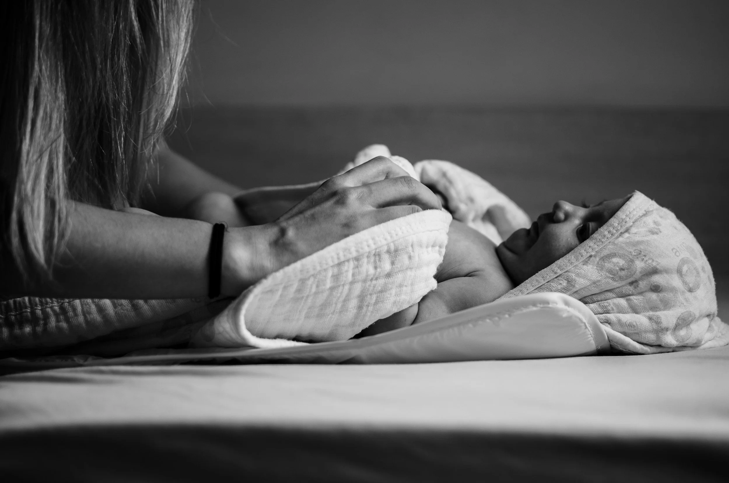 Black-and-white photo of a newborn baby lying on a hospital bed while an adult gently holds the baby’s feet.