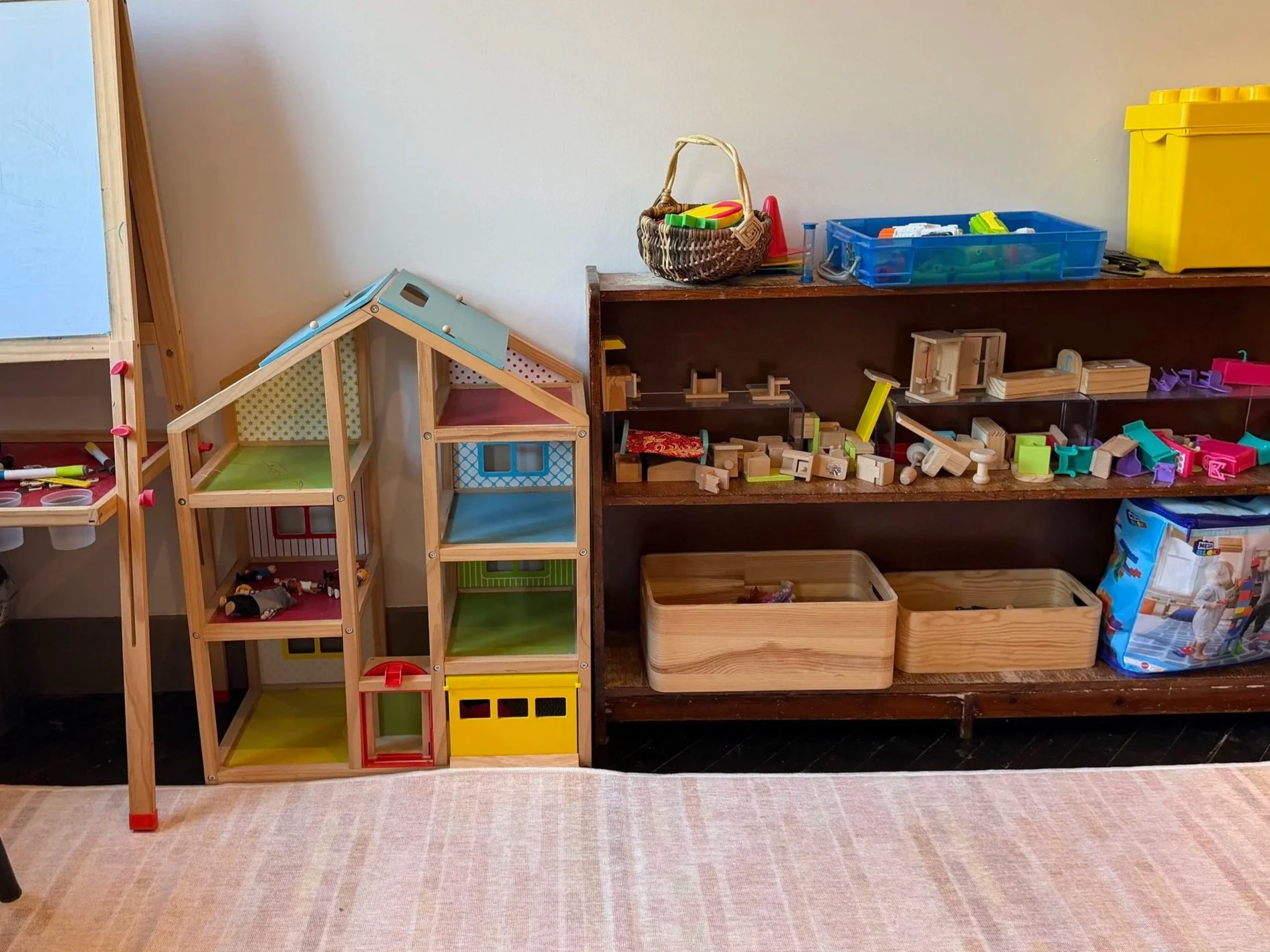 Wooden dollhouse and shelves filled with furniture, families, and other toys to facilitate children's play in the course of therapy.