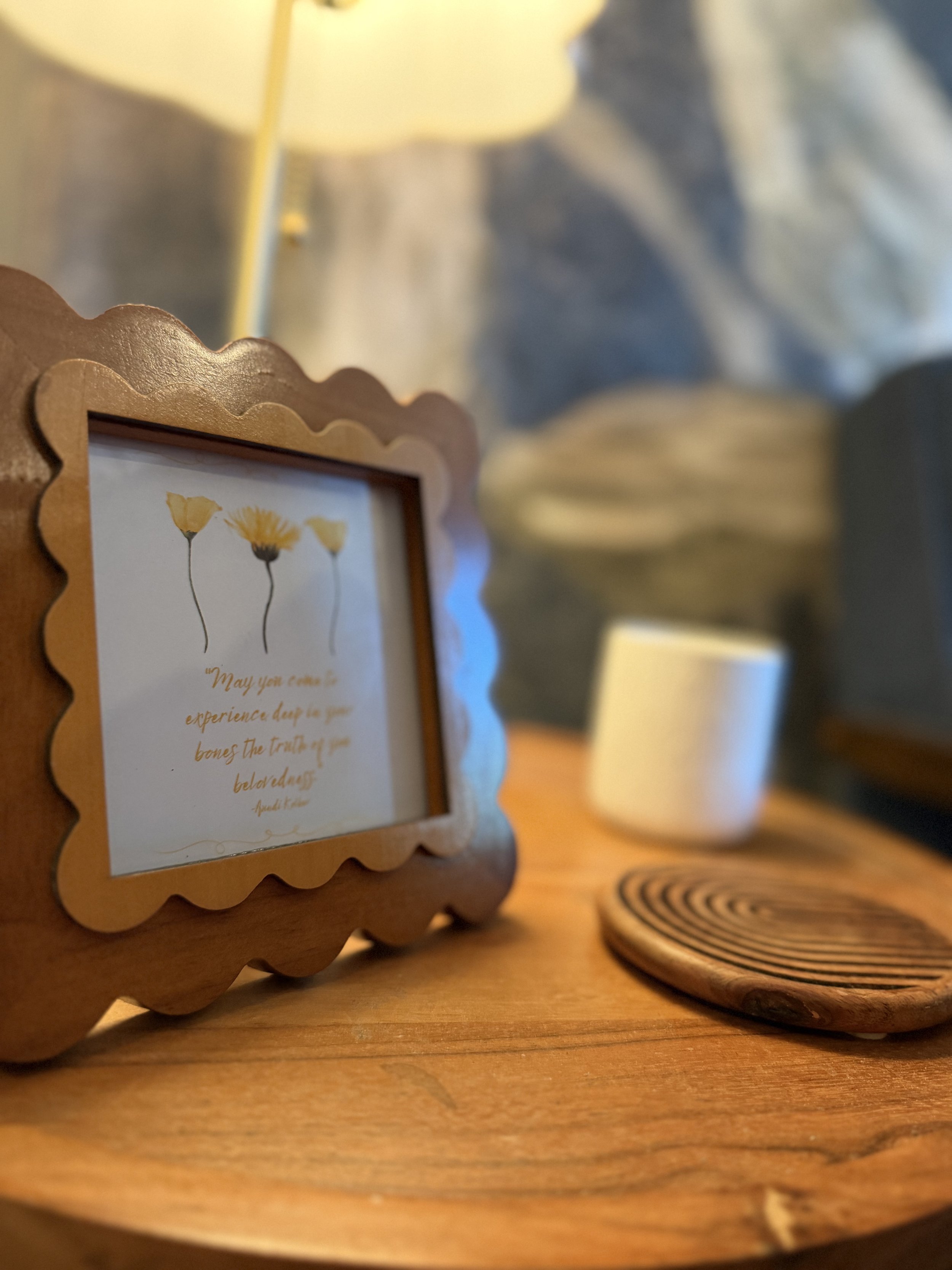 Warmly lit wooden desk with a framed floral quote, stacked books, and blurred furniture in the background