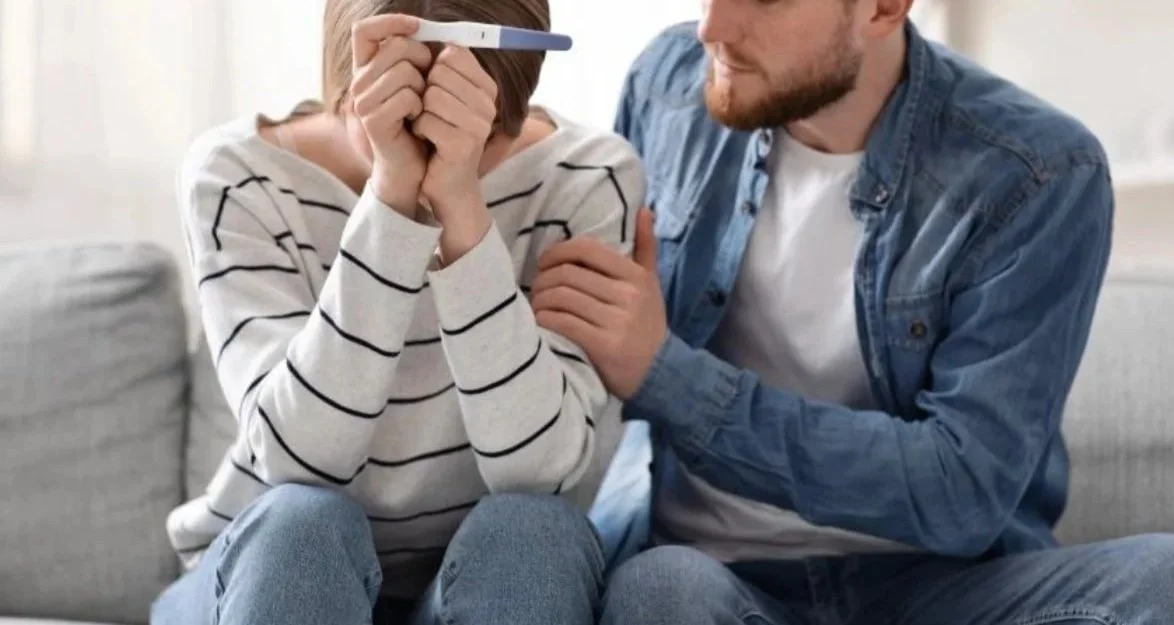 A couple experiencing infertility looks disappointed as they hold a negative pregnancy test.