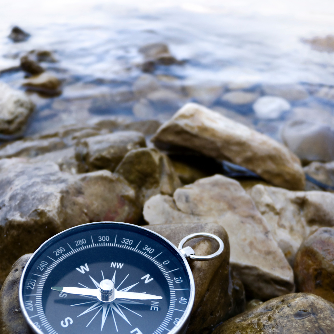 A compass resting on rocks near a body of water with gentle waves.