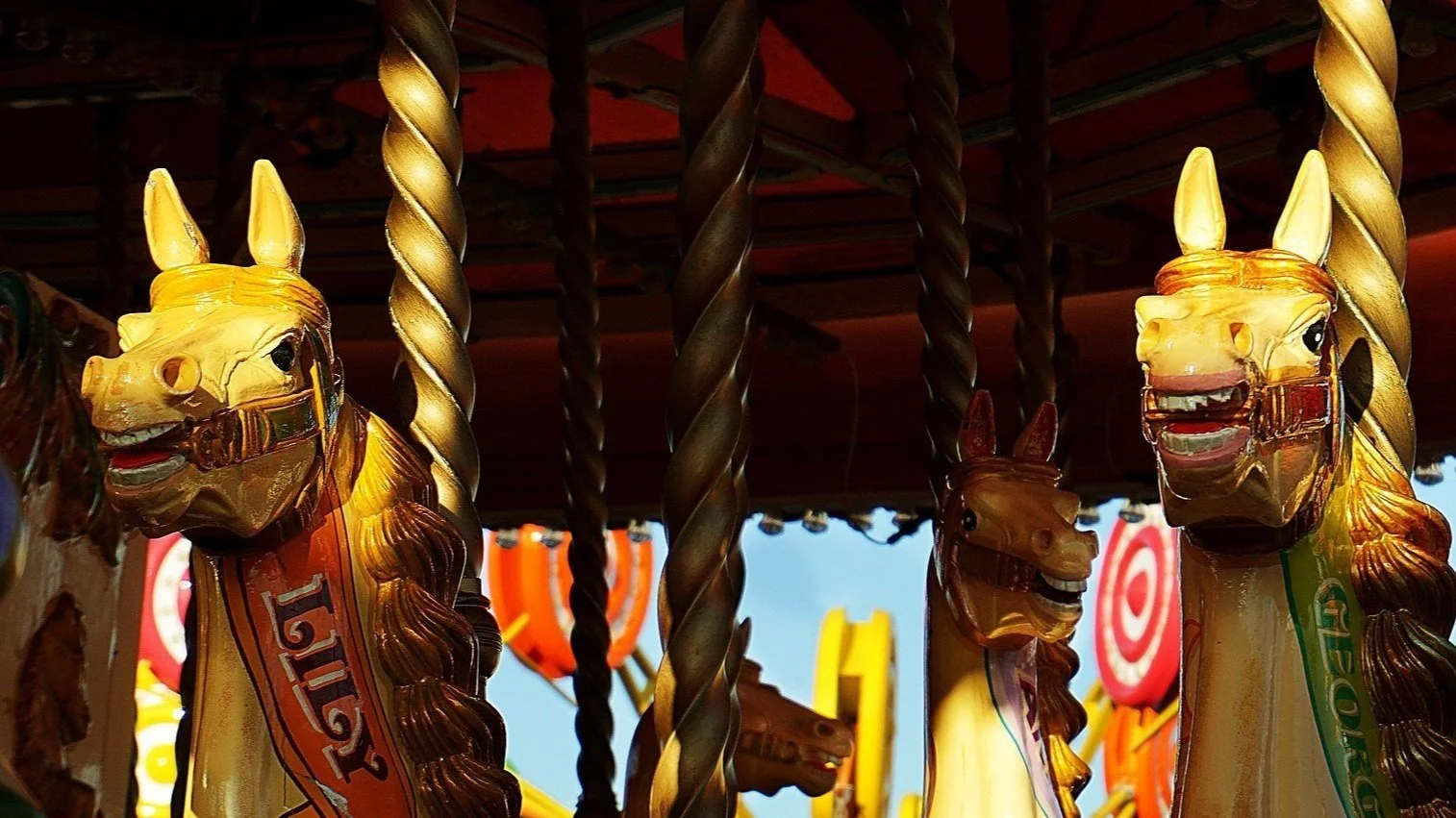 Yellow carousel horses with another carnival ride in the background
