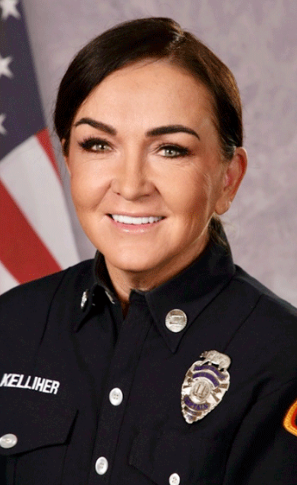 A female police officer in uniform smiling, with an American flag in the background.
