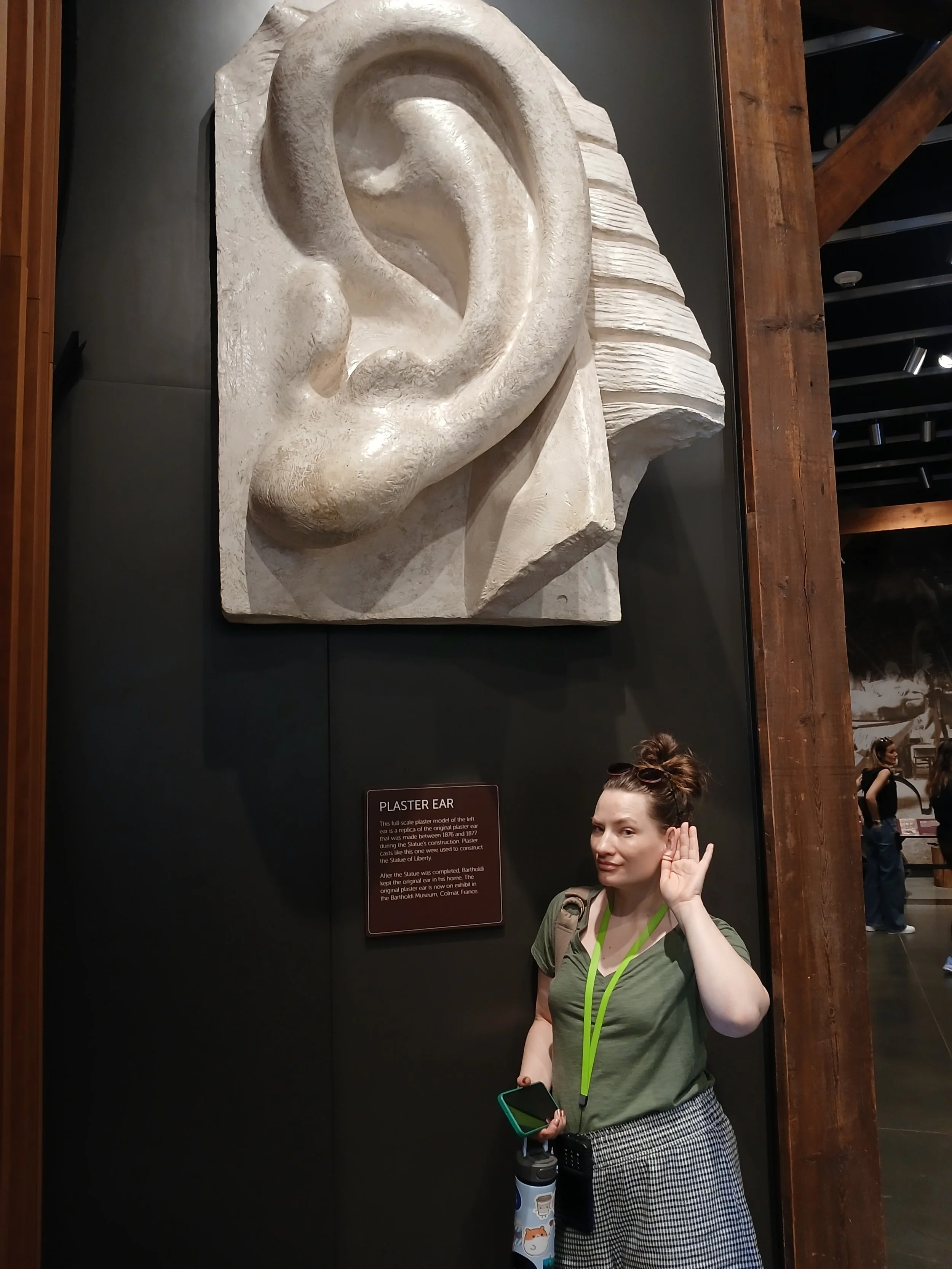 Benton's spouse posing next to a plaster mold of the Statue of Liberty's ear in the Statue of Liberty museum in New York City