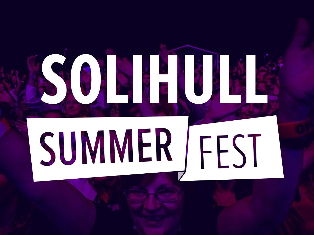 Crowd of people at Solhull Summer Fest with purple lighting, holding up hands, and smiling.