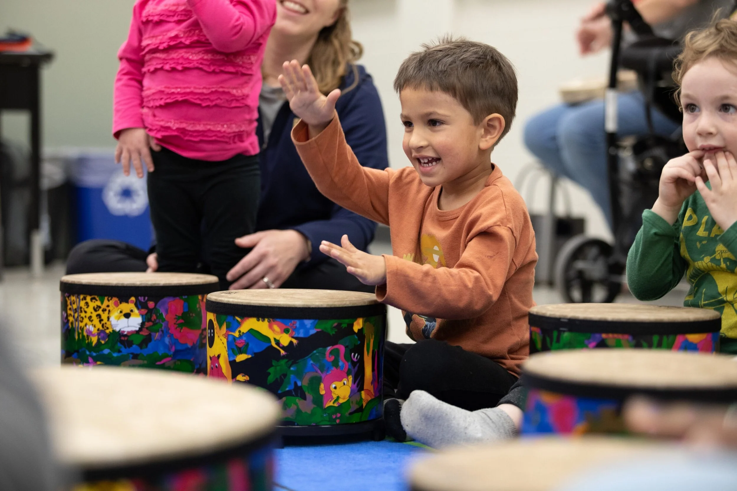 Children participating in a drumming activity, sitting on the floor with colorful drums featuring animal designs.