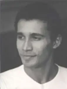 Black and white photo of a young man with short dark hair, wearing a white shirt, smiling slightly.