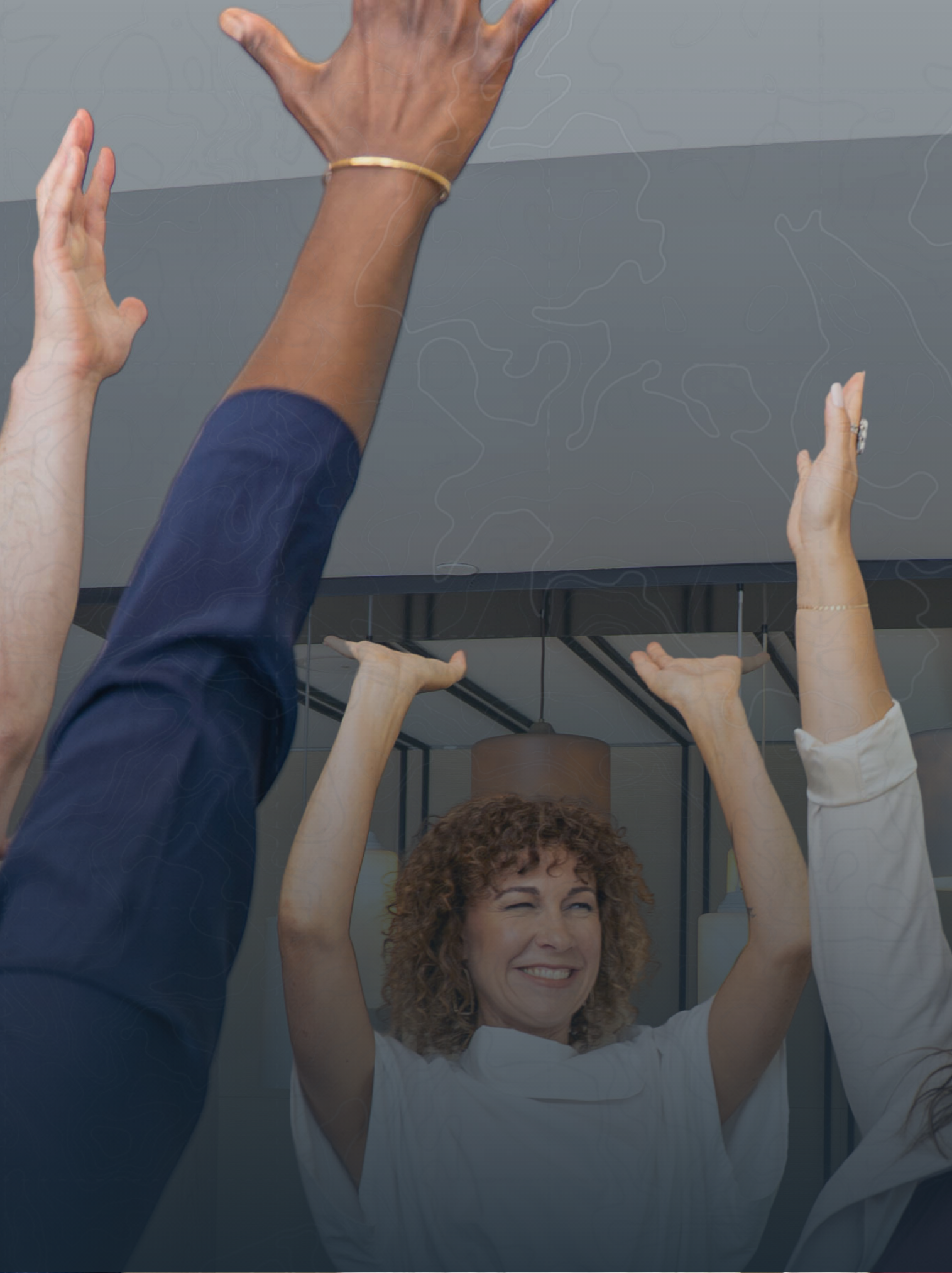 A group of people with hands raised, including a woman with curly hair and a big smile, in a bright, modern indoor setting, possibly at a meeting or event.