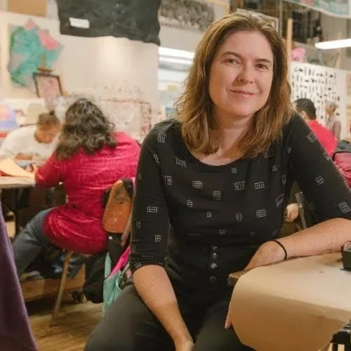 A woman sitting at a table in a classroom, with other students working behind her.