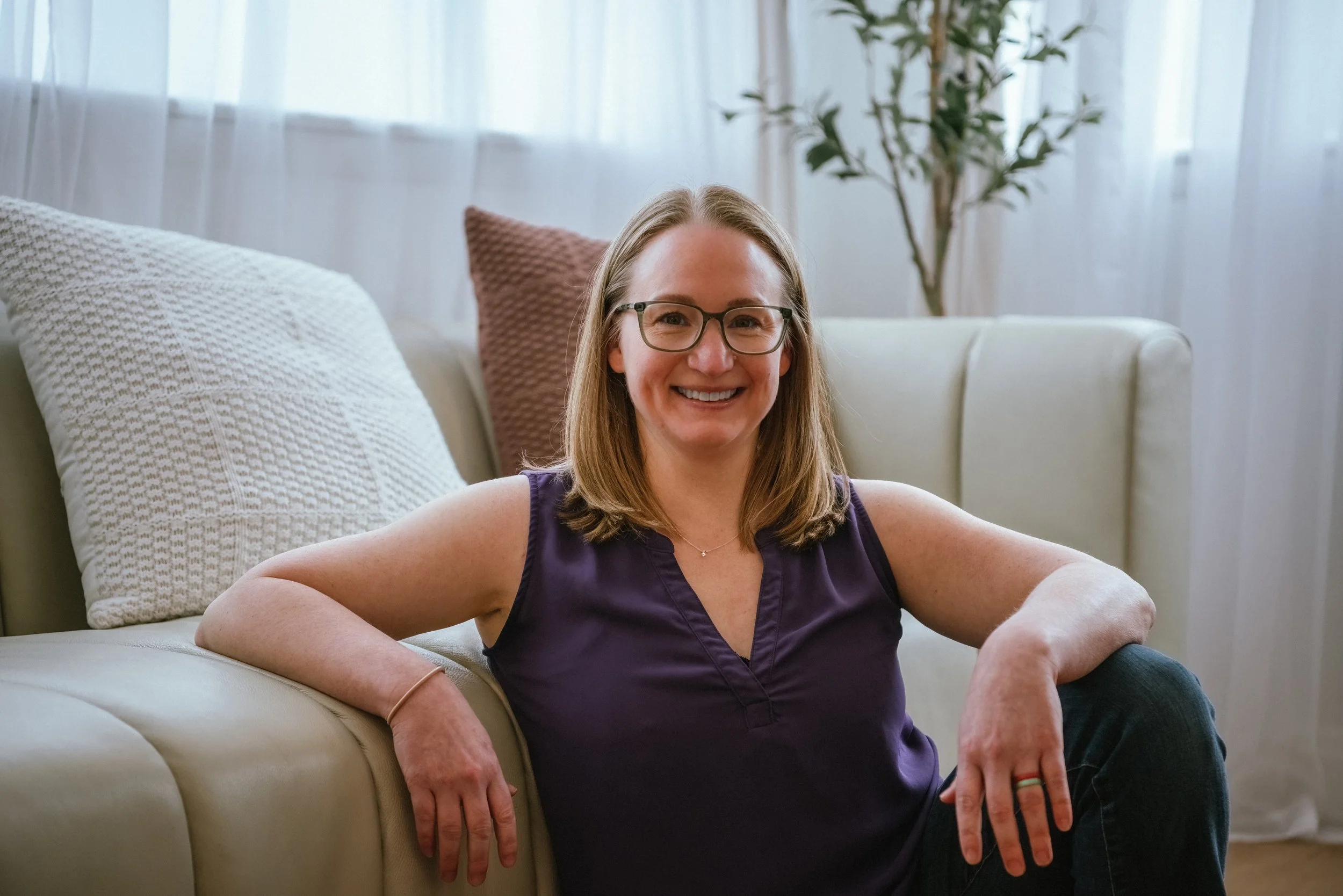 Dr Amanda Townsend sitting near a sofa in a bright living room, wearing a purple sleeveless top.