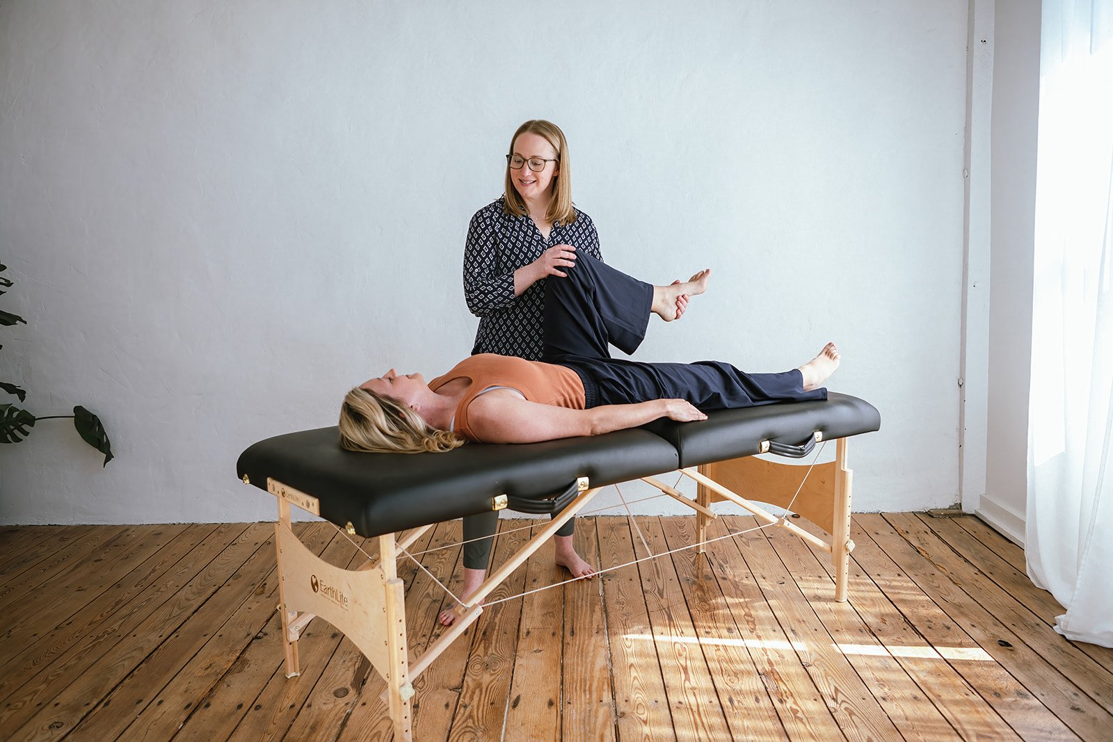 A woman lying on a black massage table while Dr Amanda holds her leg during a physical therapy session.
