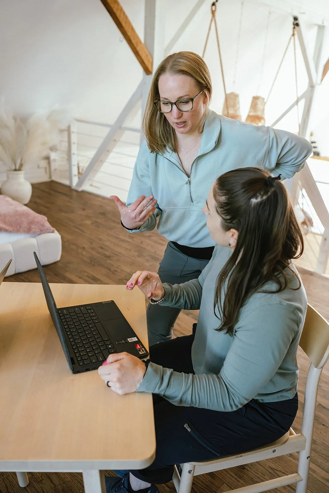Two women having a workspace discussion in a bright, cozy room at Root and Rise Consulting.