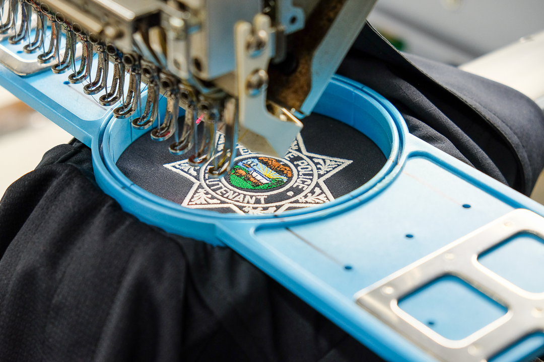 Embroidery machine stitching a police badge patch onto black fabric.