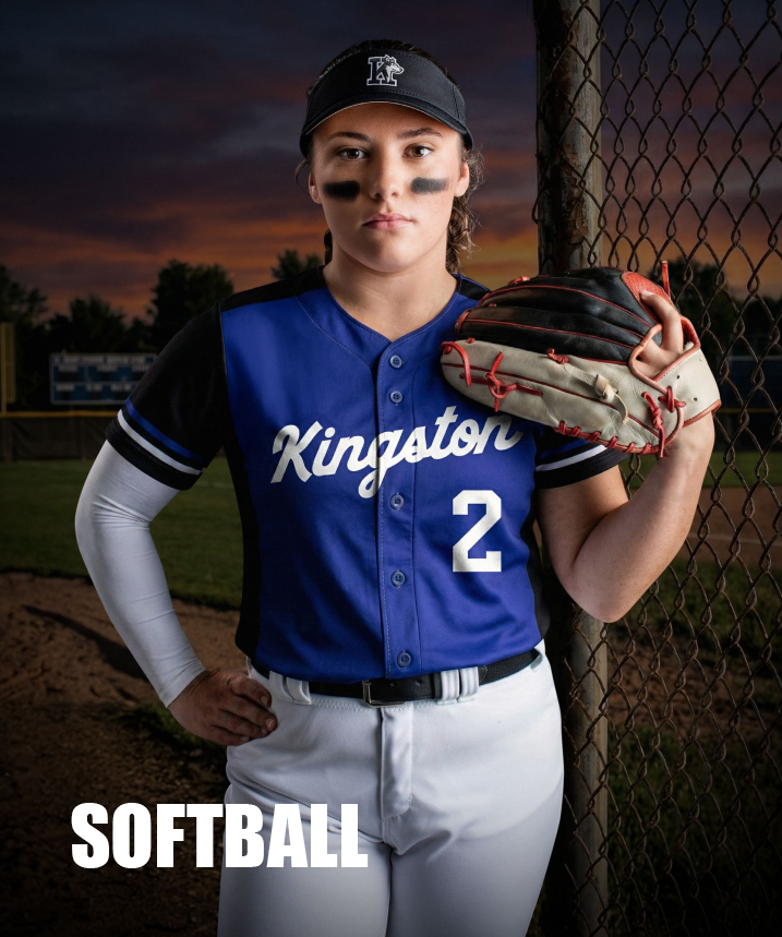 A female softball player standing on a baseball field at sunset, wearing a blue jersey , a black cap, holding a softball glove, with a serious expression.