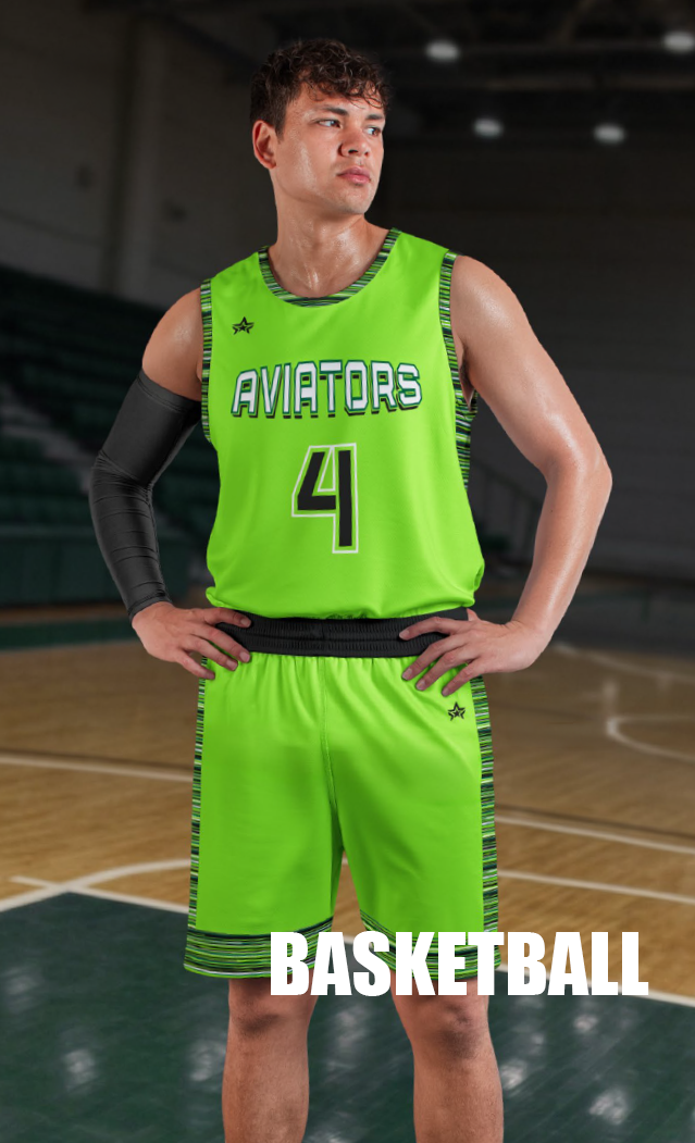 A young male basketball player stands on an indoor basketball court wearing a bright green uniform . He has a black arm sleeve on his right arm and his hands on his hips, looking to the side.