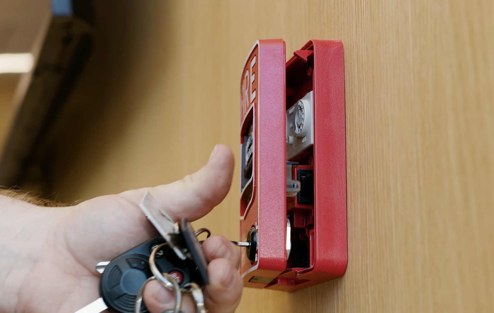 Close-up of a hand inserting a key into a red lockbox on a wooden surface.