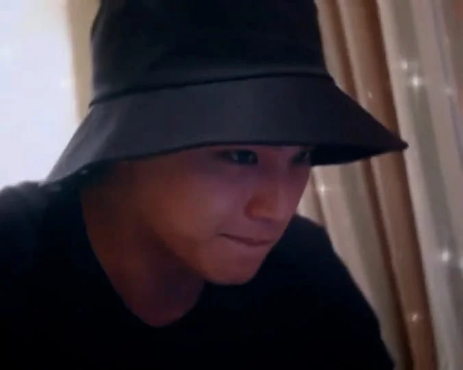 Person wearing a black bucket hat and black shirt looking down with a focused expression.