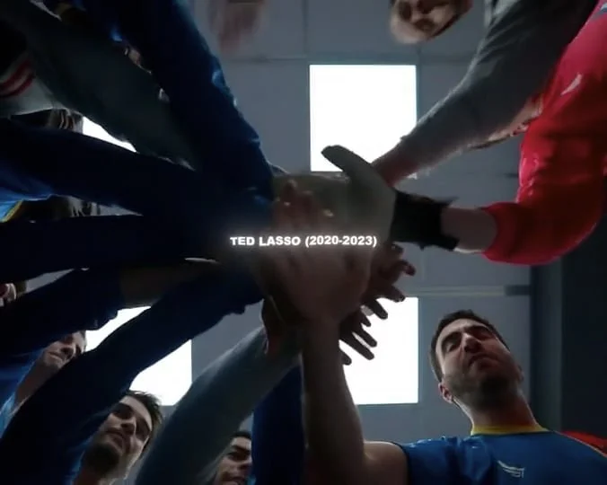 A group of people putting their hands together in a huddle, smiling and showing team spirit, in a sports setting.