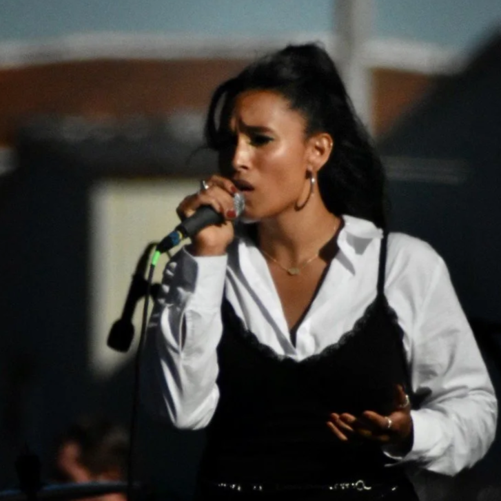 Leah Lahkiah singing into a microphone during a performance at Kentucky's 2022 NULU Festival  wearing a white shirt and black dress with long earrings.