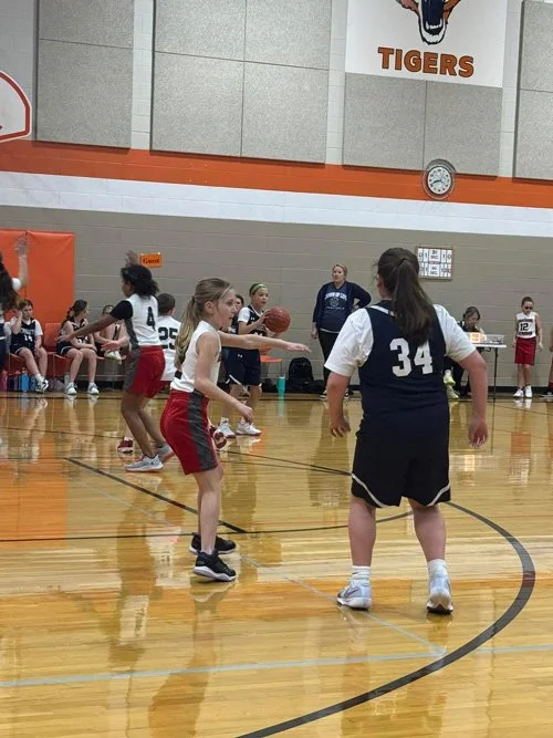 Young girls playing basketball in a gymnasium during a game.