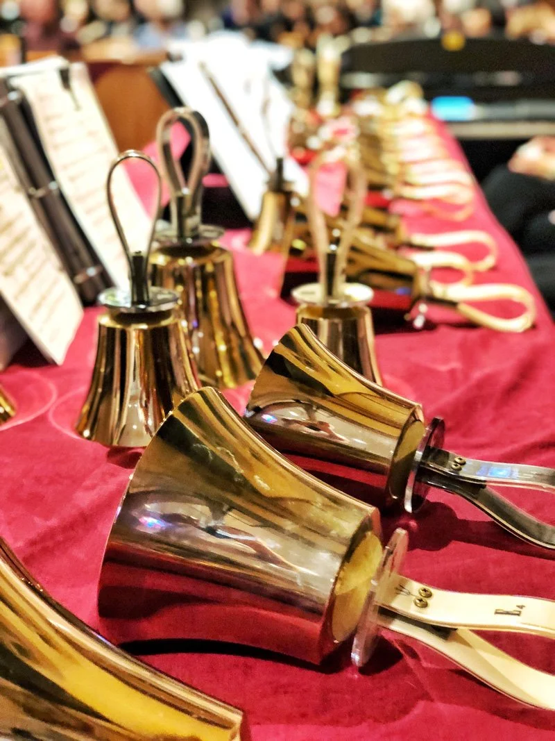 A display of shiny brass bells on a red cloth table at an auction or sale event.