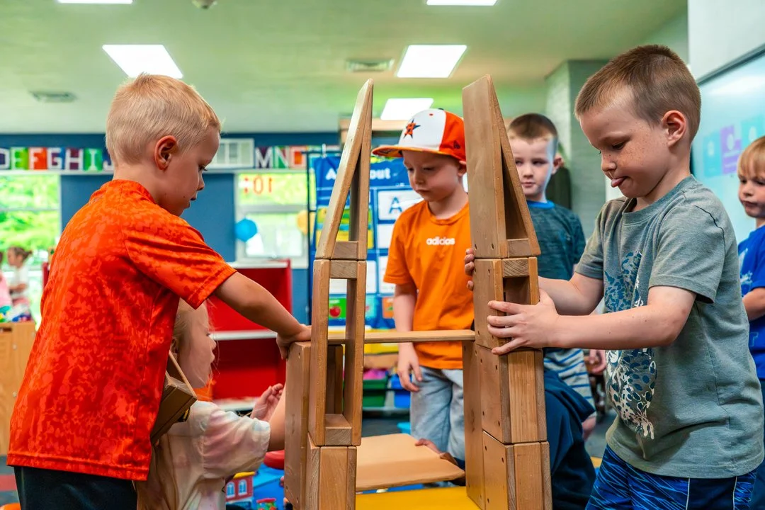 Children playing with wooden blocks in a classroom.