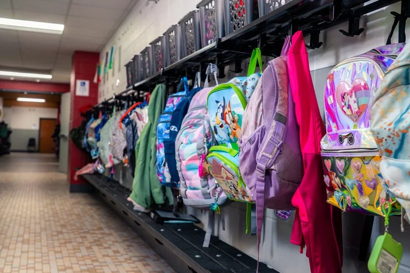 School backpacks hanging on hooks in a hallway