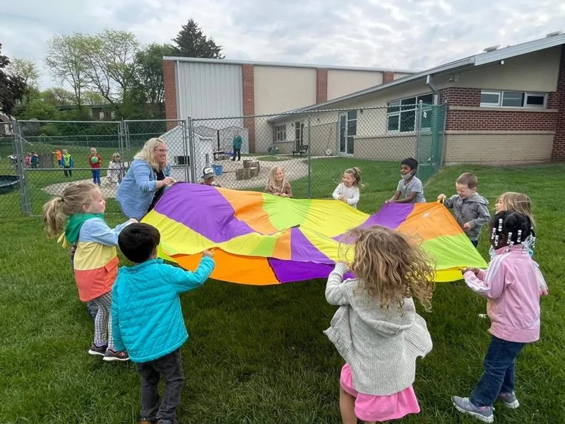 Children and a woman holding a colorful parachute outdoors.