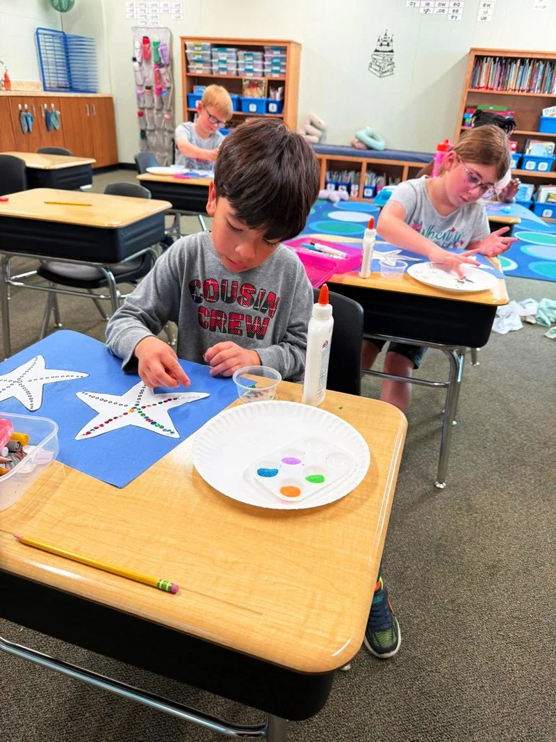 Children in a classroom decorating star-shaped cutouts with colorful dots.